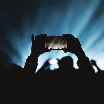 Silhouetted hands holding a smartphone recording a bright stage scene.