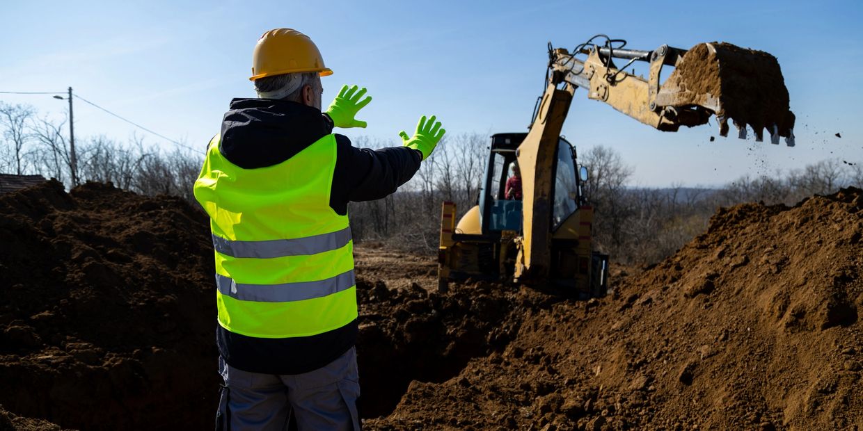Construction worker guiding an excavator digging soil at a site.