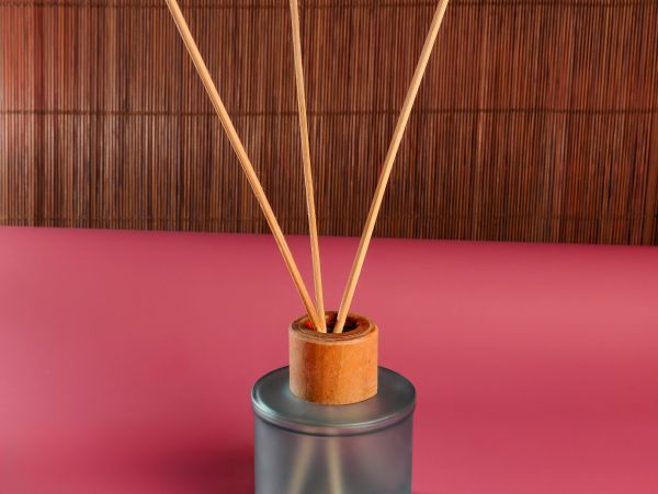 A reed diffuser with wooden sticks on a pink surface and bamboo background.