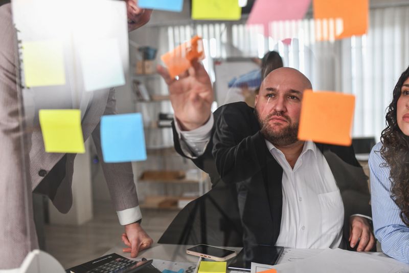 Business team collaborates in a modern office, planning and brainstorming ideas using colorful sticky notes on a glass office wall during an intense meeting focused on strategy and teamwork.