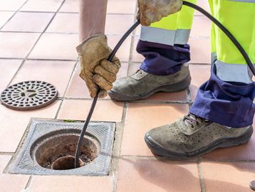 Worker cleaning a drain with a tool.