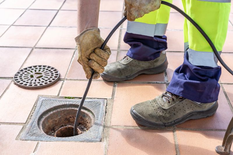 Close-up of sewer worker unclogging blocked yard drain with high pressure water jetting hose.