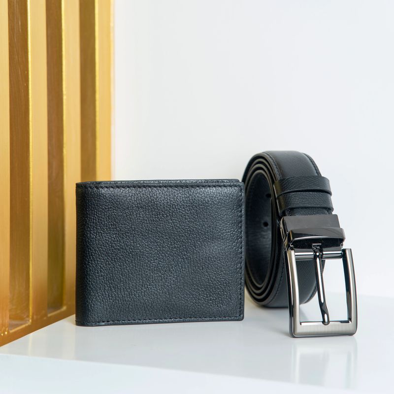 A stylish black leather wallet and matching belt with a sleek silver buckle, placed on a white surface with a wooden panel in the background, perfect for fashion or lifestyle concepts.
