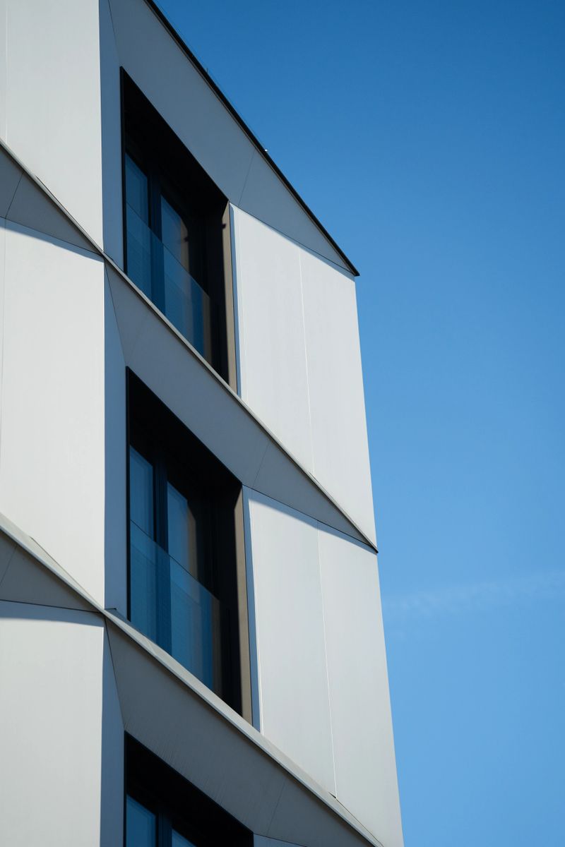 Geometric white facade of a modern building with large windows and sharp lines, set against a clear blue sky. Suitable for illustrating contemporary architecture, urban design, or real estate concepts.