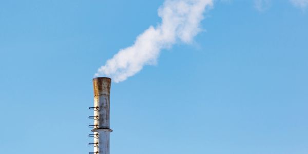 Industrial chimney releasing white smoke against a clear blue sky.
