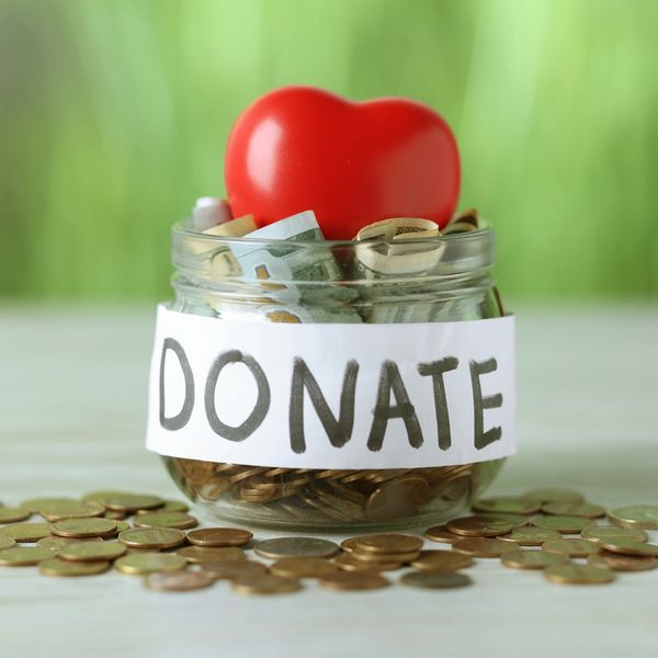Donation jar filled with money and a red heart on top.