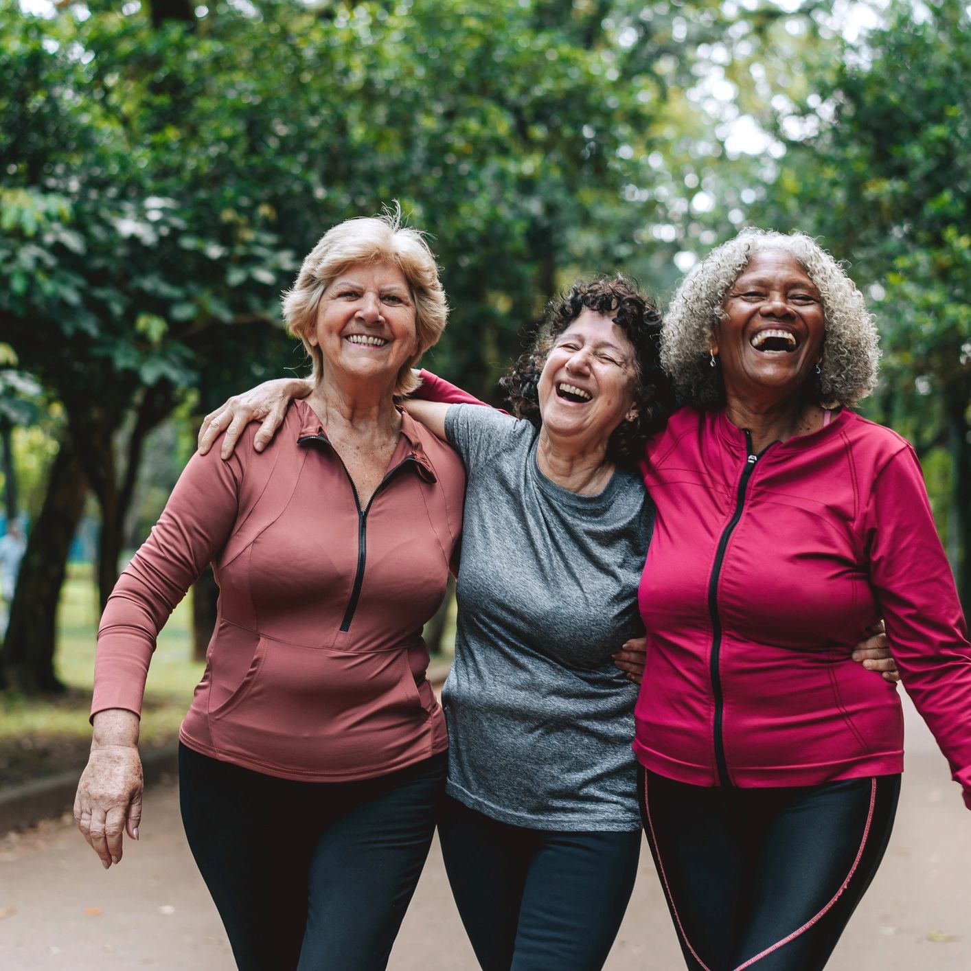 Three older women joyfully walking arm-in-arm outdoors.
