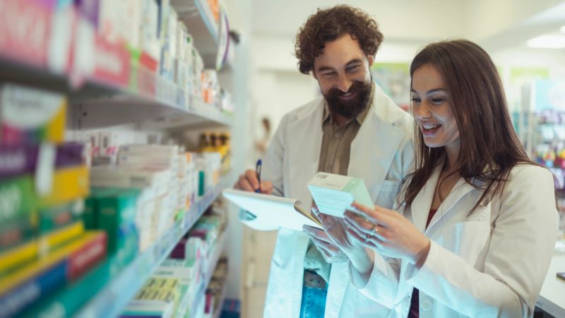 Male and female pharmacists diligently examine medications in a brightly lit pharmacy