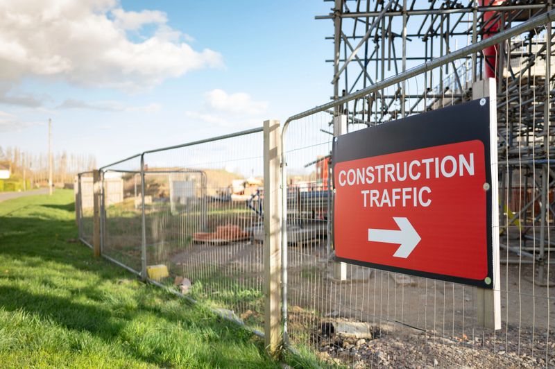 Large Construction Traffic sign attached to a metal fence seen at the perimeter of a housing development project in the UK. Both affordable and large private homes are being built here.