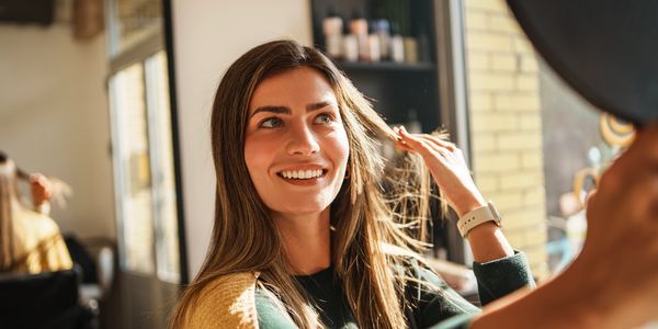 A smiling woman admiring her hair in the mirror at a salon.