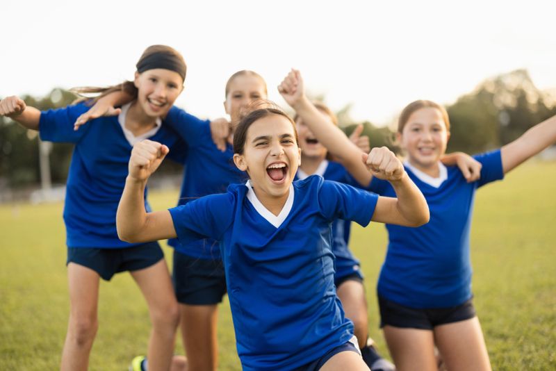 Girls soccer team celebrating victory on field. Young teammates showing happiness after scoring a goal or winning game