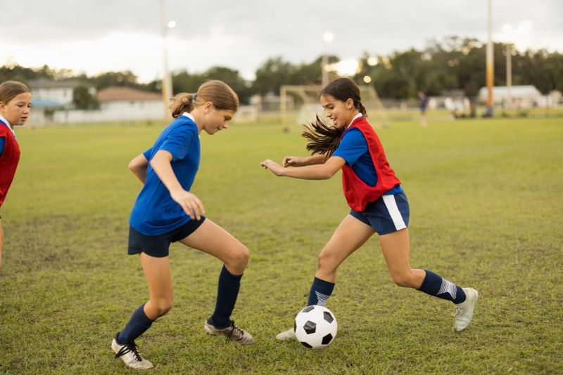 Girls playing soccer on a grassy field, actively dribbling the ball and competing during team training