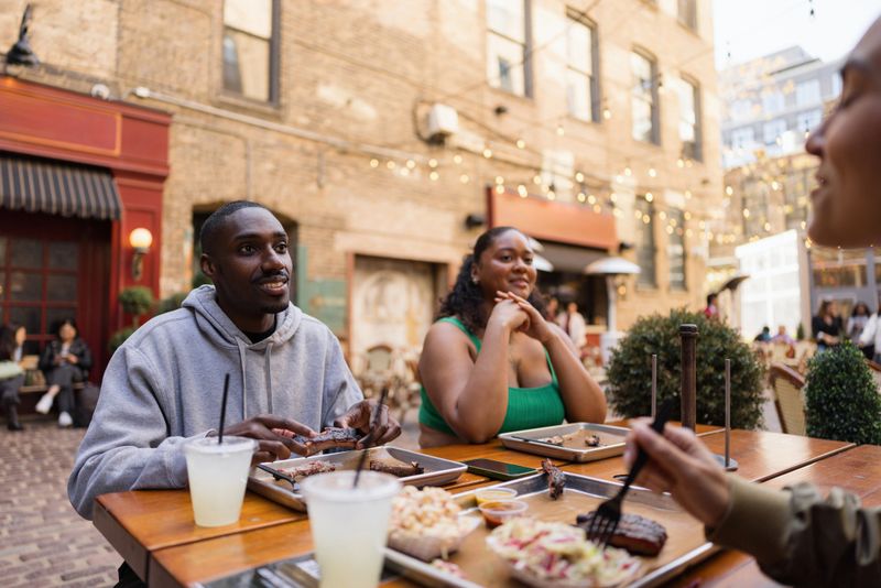Diverse friends sharing a casual American barbecue meal and lemonade at an outdoor restaurant patio with string lights