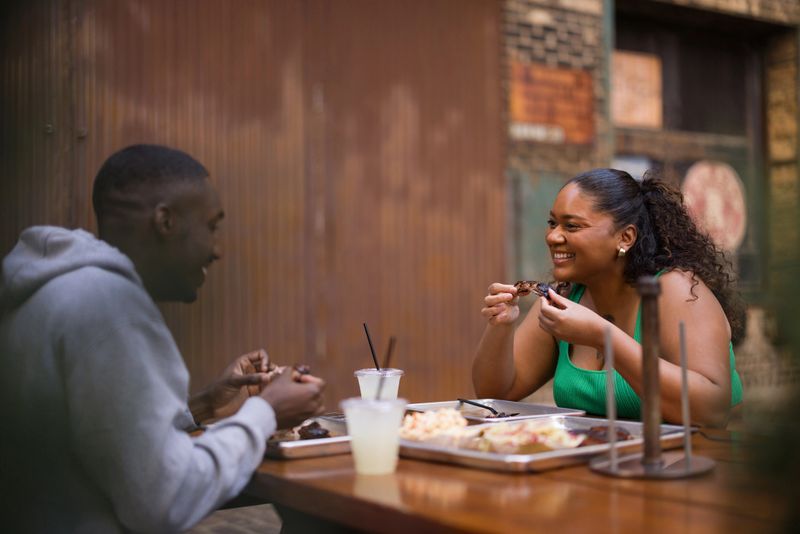 Happy diverse couple enjoying BBQ ribs and drinks at an outdoor restaurant, sharing a fun meal together