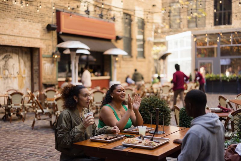 Diverse friends enjoying lunch and conversation at an outdoor restaurant patio in a city, experiencing urban social lifestyle