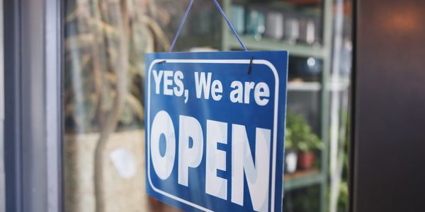 Blue sign saying 'YES, We are OPEN' hanging on a glass door.