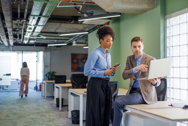 Group of diverse professionals collaborating and brainstorming together on a laptop, promoting teamwork and creativity in a modern office space