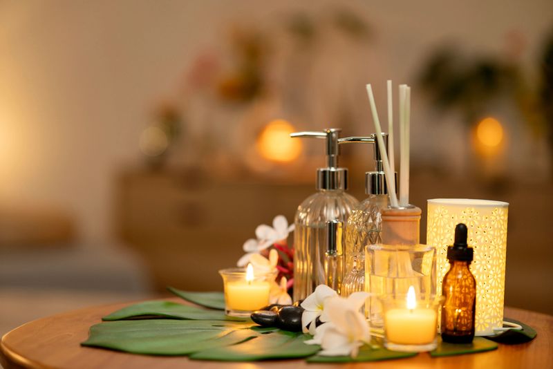 Soothing spa setup features glowing candles scented oils decorative diffuser frangipani blossoms smooth stones on a wooden table inviting tranquility calm wellness