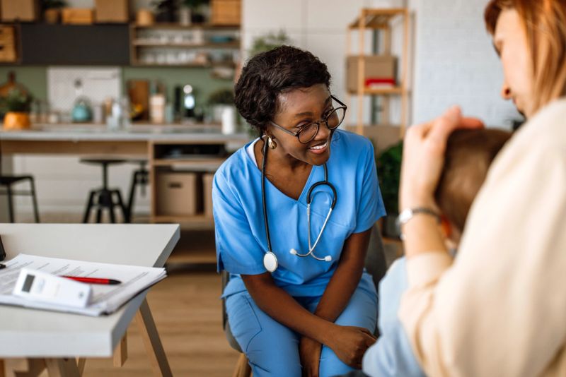 Female pediatrician at home visit examining little boy, while mother is holding him.