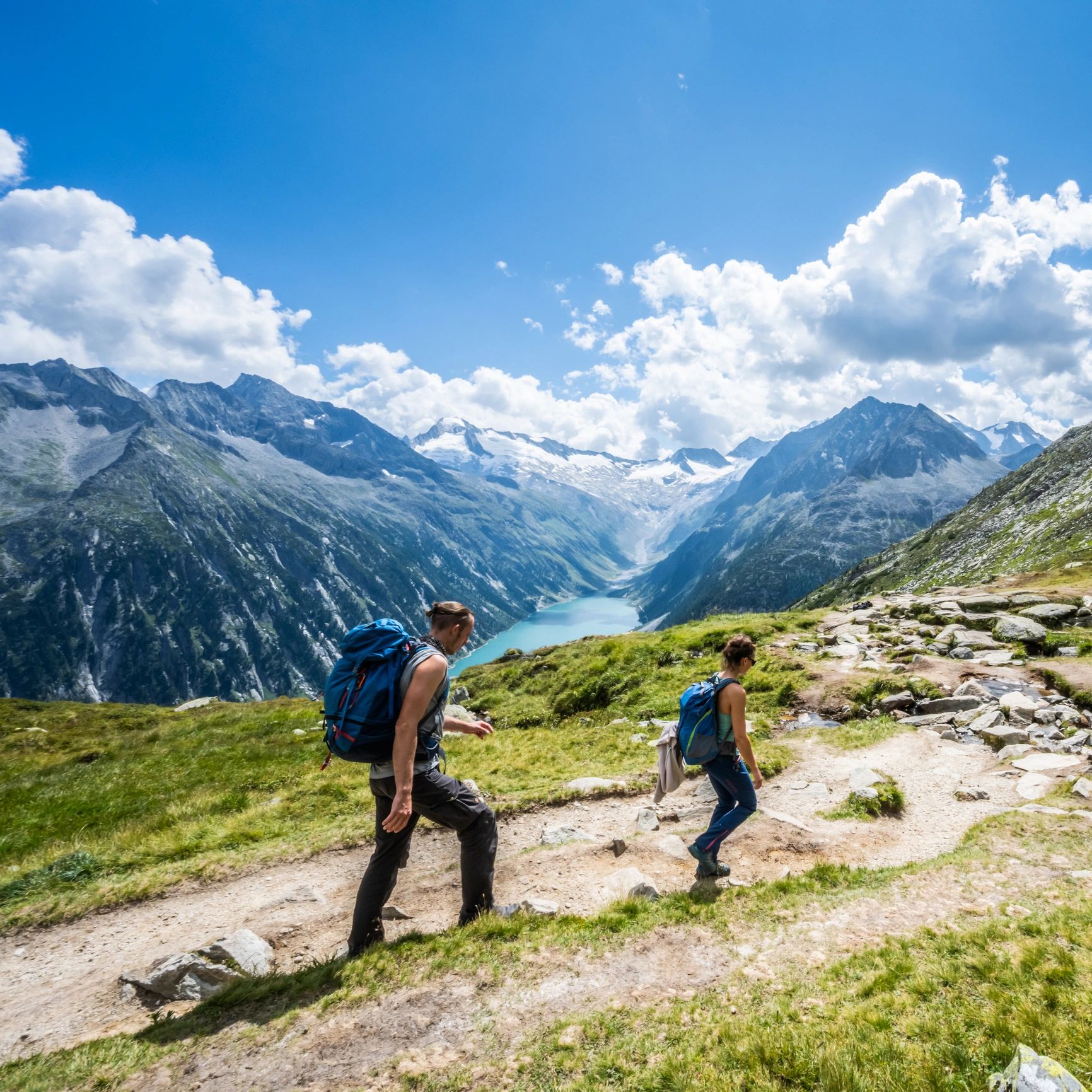 Two hikers trekking along a mountain trail with scenic views.