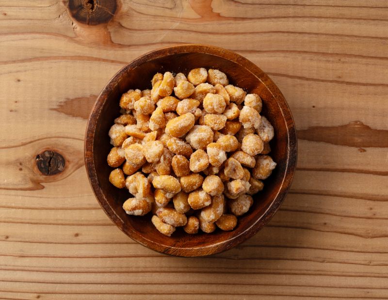 Top view of honey roasted peanuts in a wooden bowl on a wooden table