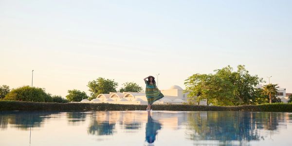 Woman standing near a reflective water surface at sunset.