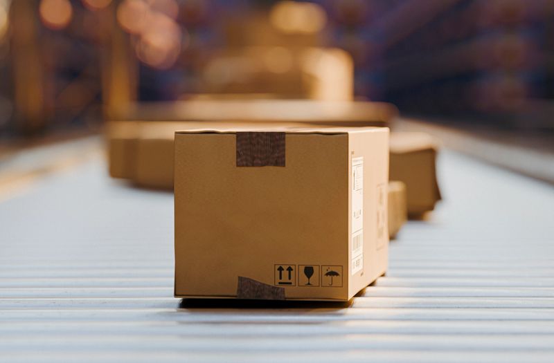 Cardboard package traveling on a conveyor belt inside a busy distribution warehouse, highlighting shipping, logistics, order fulfillment, automation and efficient parcel handling for ecommerce and supply chains.