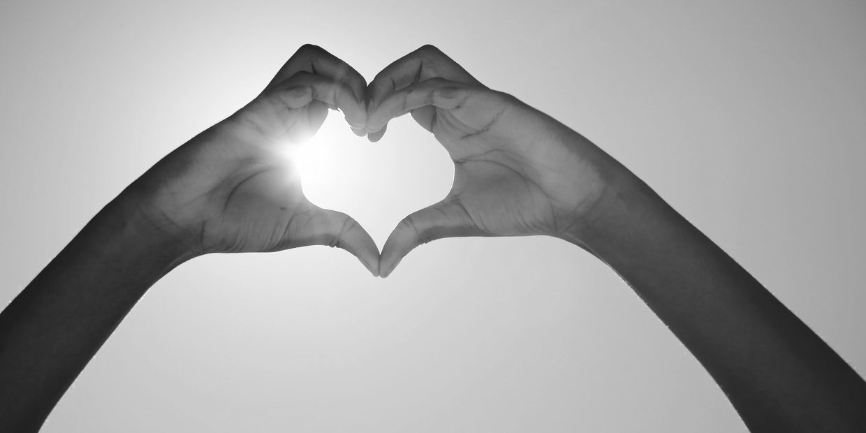 Hands forming a heart shape against the sunlit sky.