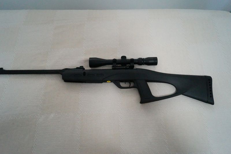 Close up of a powerful synthetic black airgun, featuring a textured grip, a long steel barrel, and a mounted optical sight.
