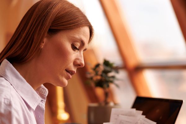Woman reviewing receipts at a desk with a laptop and smartphone.