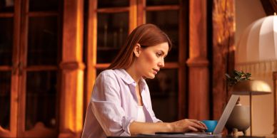 Woman working on laptop in cozy wooden room.