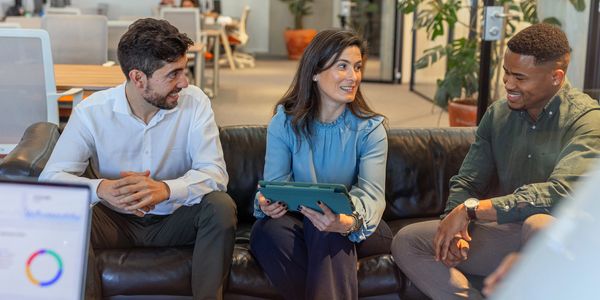 Three colleagues engaging in a lively discussion on a couch in a modern office.