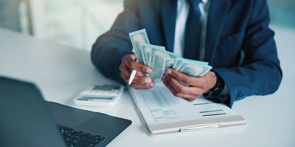 Person counting US dollar bills at a desk.