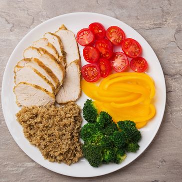 Healthy plate with chicken, quinoa, tomatoes, bell peppers, and broccoli.