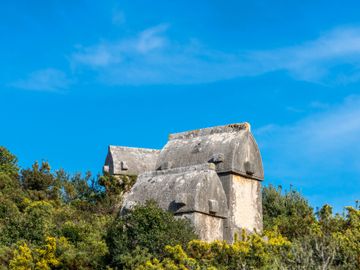Unique old stone structures with rounded roofs amidst greenery under a blue sky.