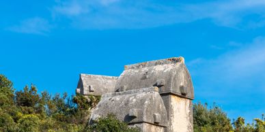 Ancient stone tombs on a green hill under a bright blue sky.