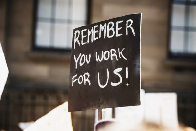 Protest sign reading "Remember you work for us!" held up outdoors.