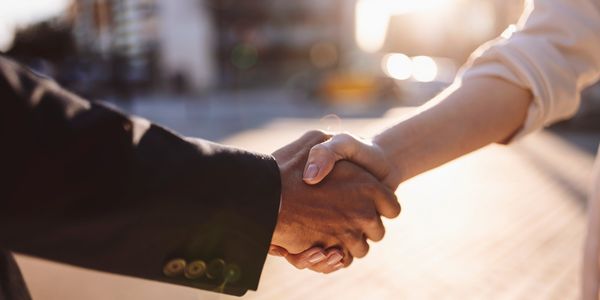 Two people shaking hands in a sunlit outdoor setting.