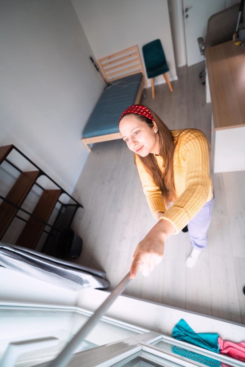 Natural daylight fills the room while woman cleans windows, representing home care, organization, and renewal.