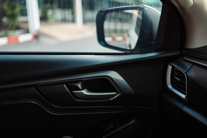 Close-up shot of a modern car interior focusing on the black leather door panel, silver door handle, and side view mirror. The image highlights vehicle ergonomics, automotive design, and transportation aesthetics.