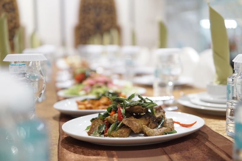 Food dish featuring savory meat with green herbs and red chili served on a white plate at a catered event with water bottles and glasses