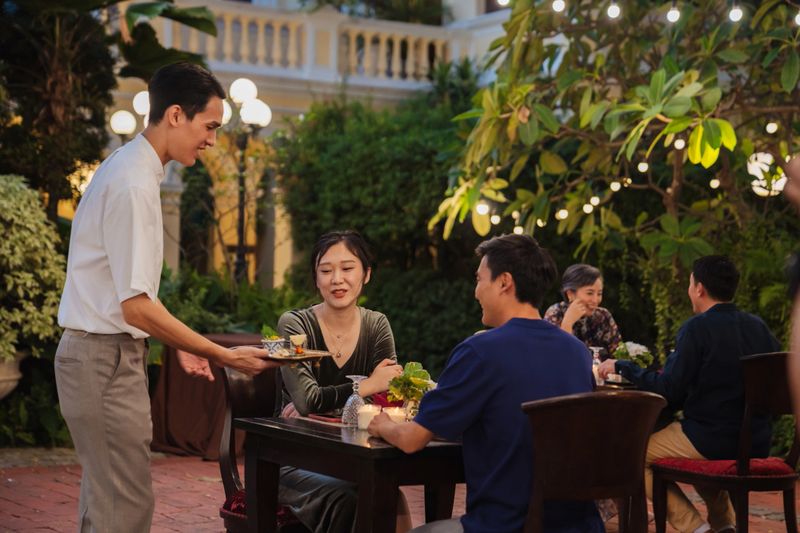 Waiter is serving bar snacks to a smiling, young couple in a beautiful outdoor restaurant.