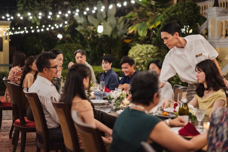 A large family enjoying dinner together at a long table in an elegant outdoor setting, sharing conversation and a meal in a warm evening atmosphere.