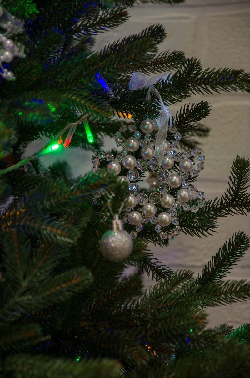 Close-up of a decorated Christmas tree featuring a pearl and crystal snowflake ornament with colorful lights and a glitter ball.