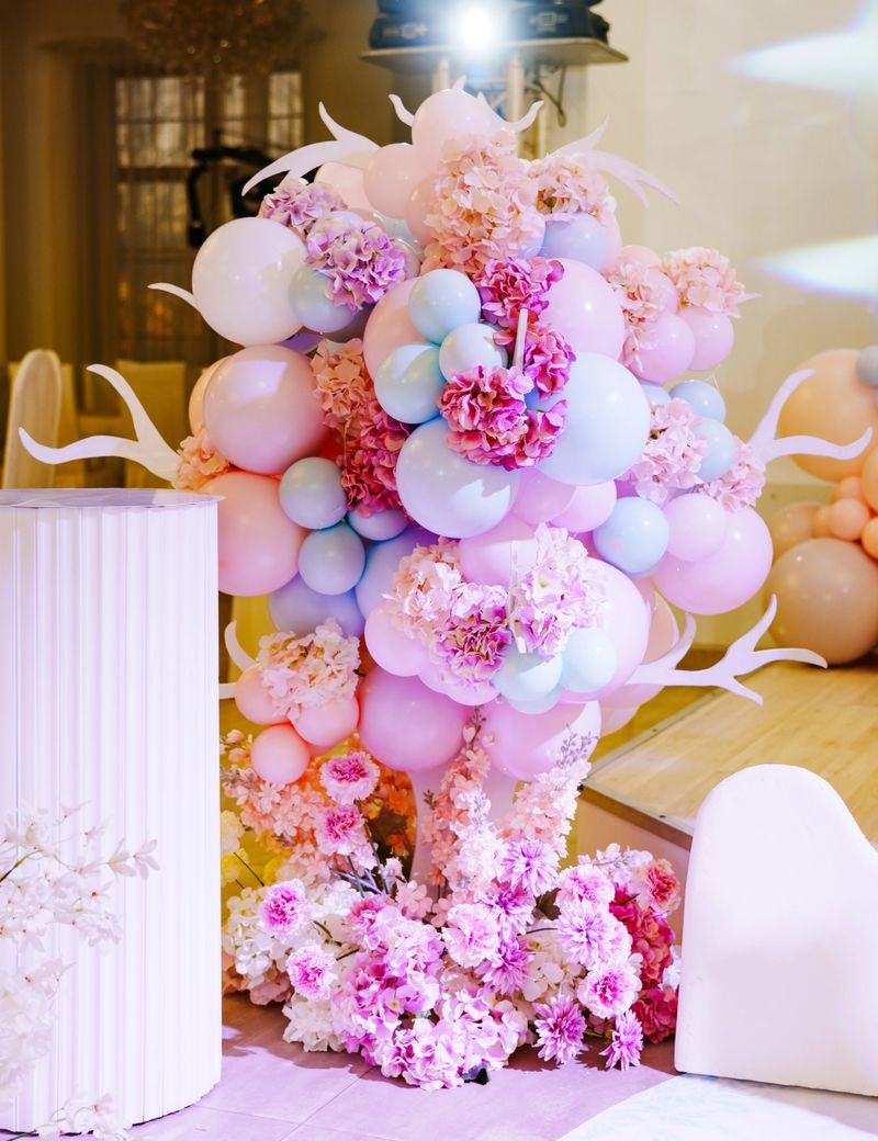 A display of colorful balloons and flowers fills the room. The balloons are in shades of pink and blue. The arrangement adds a festive feel to the venue.