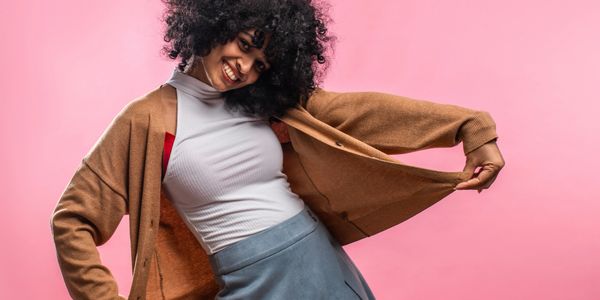 Joyful woman dancing with a big smile against a pink background.