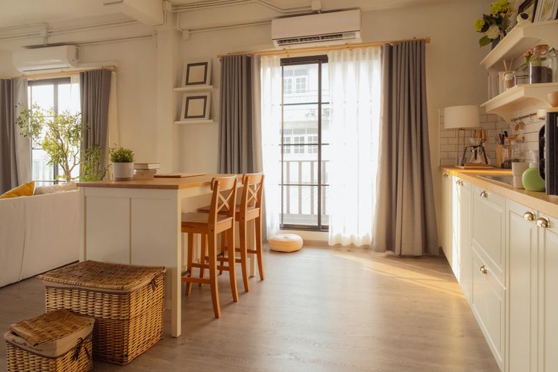 Bright modern kitchen and dining area with wooden chairs and island table in cozy apartment interior, natural sunlight through window creating warm minimalist home lifestyle and stylish domestic space.