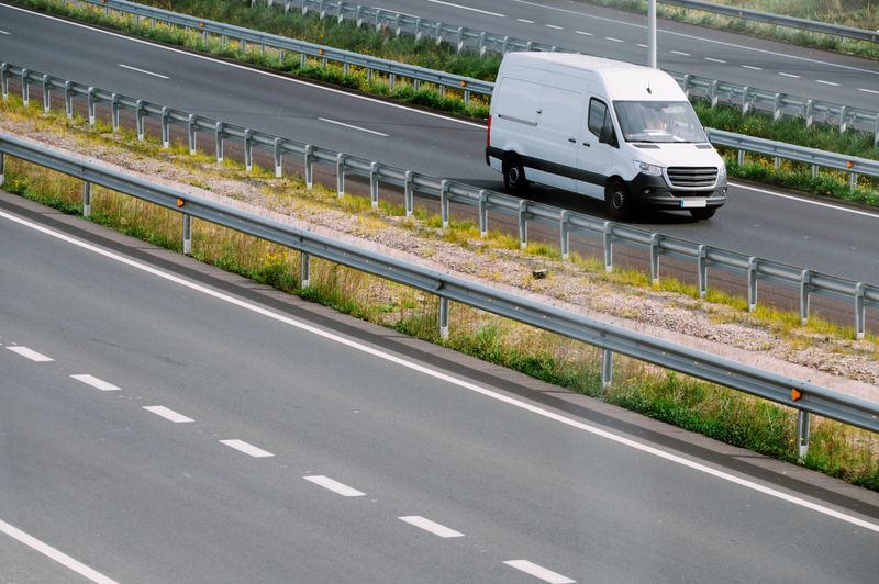 White commercial van driving along a highway, representing goods transport and logistics services.