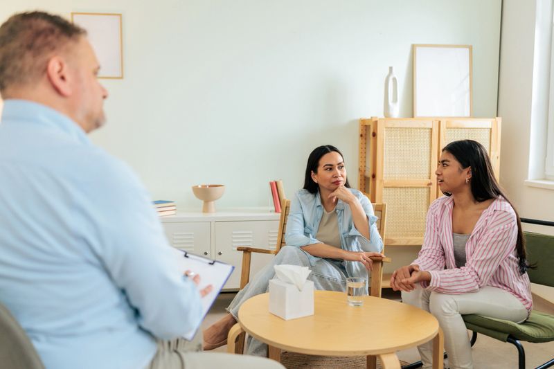 Mother and teenage daughter sitting together during a psychotherapy session while speaking with a therapist in a calm counseling office. The scene reflects family therapy, emotional support, and mental health care.