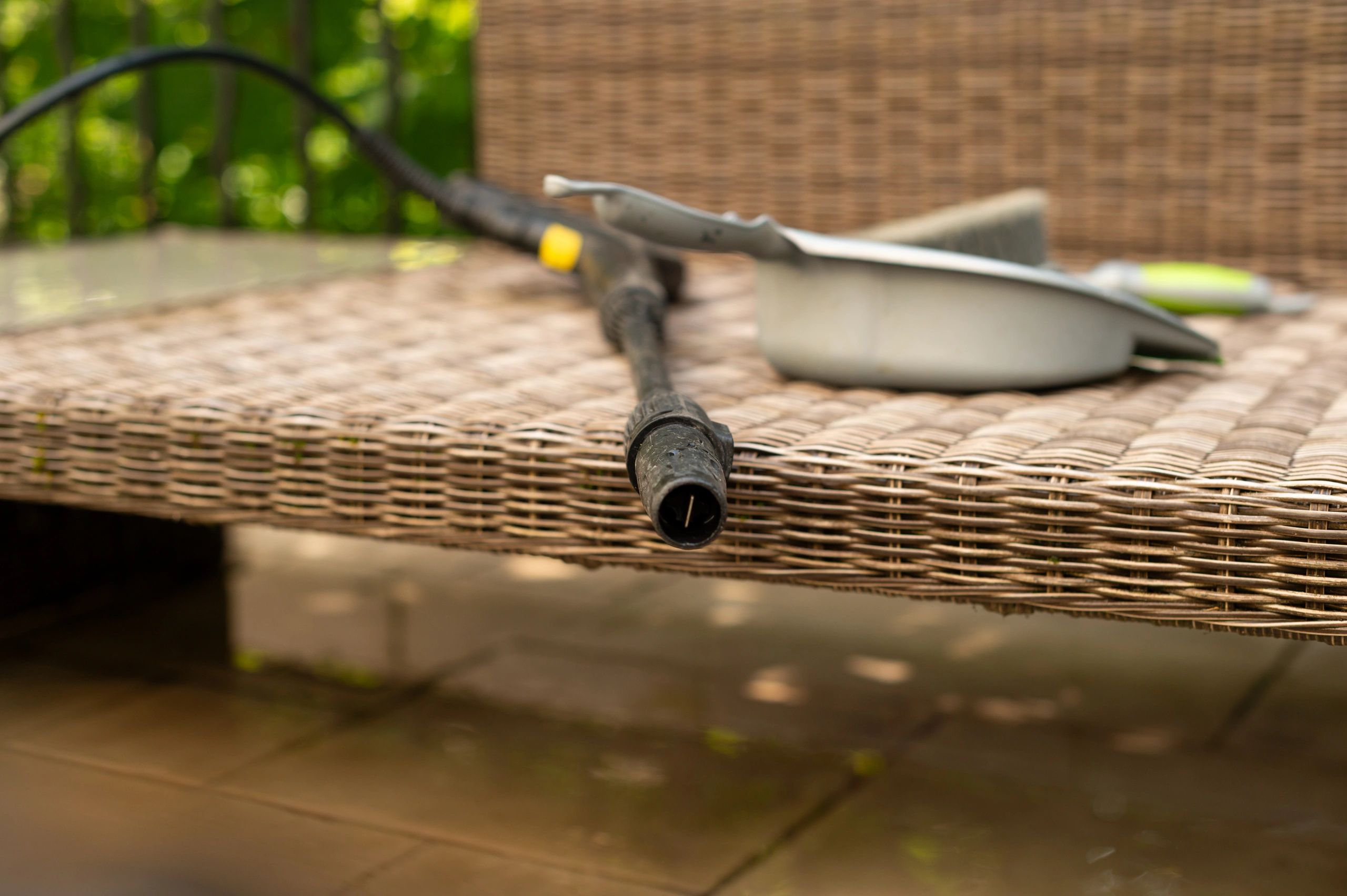 A pressure wash nozzle and cleaning tools on a wicker bench.